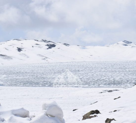 Frozen Sheosar lake starting to melt in June with snow covered mountains in the background