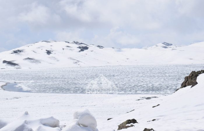 Frozen Sheosar lake starting to melt in June with snow covered mountains in the background